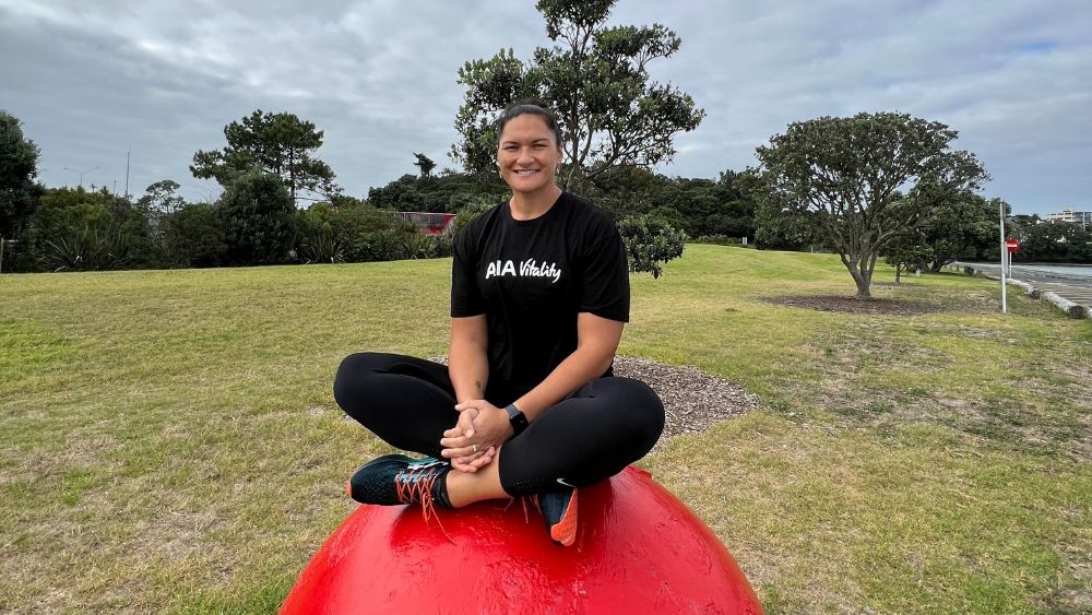 Image of Dame Valerie Adams sitting on boulder at a park wearing AIA Vitality shirt.