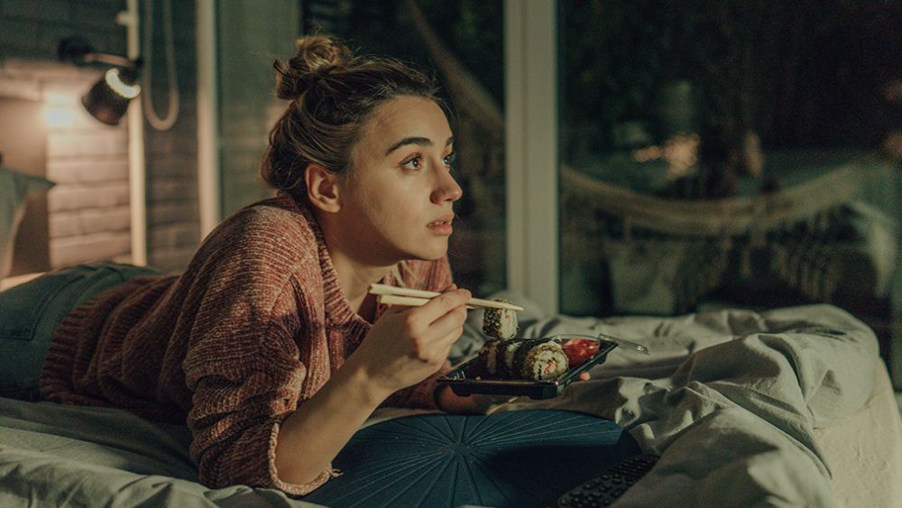 Person eating sushi while lying down in bed