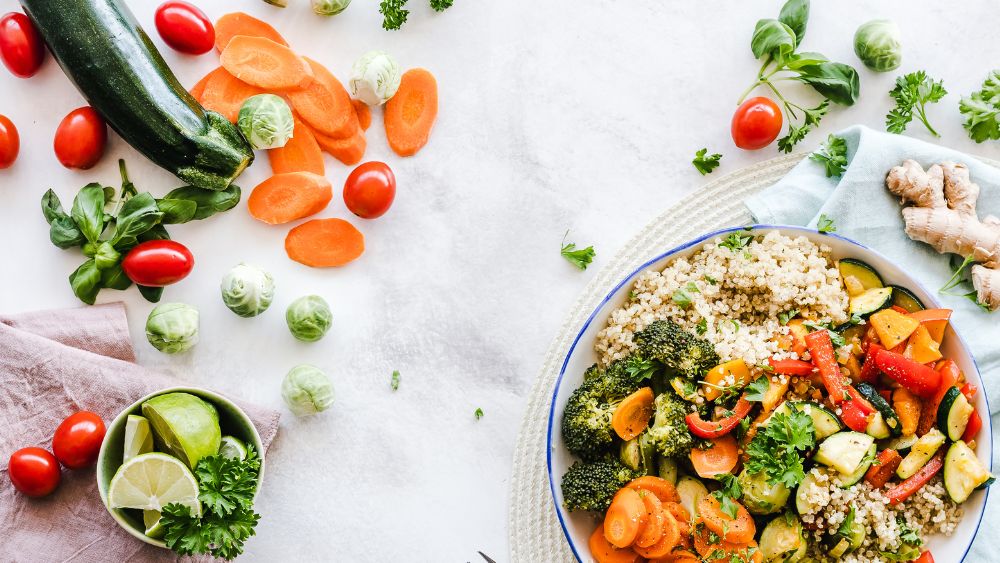 Plate of fresh vegetables next to ginger, chopped carrots, basil, brussel sprouts, tomatoes, and limes.