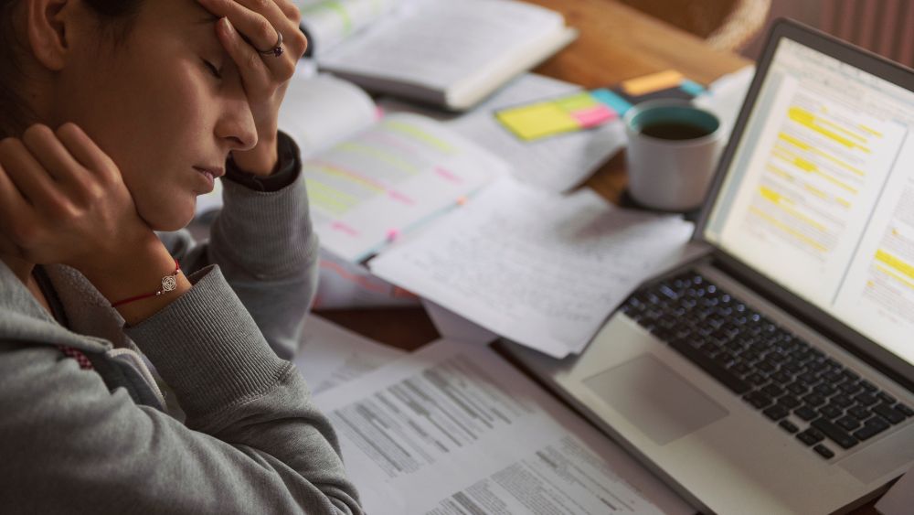 Person with lots of paperwork and laptop on desk in front of them